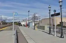 A train platform with concrete pavement, street lamps, signage, and a ramp for wheelchair access