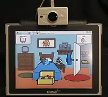 A screen showing a stylised version of a bedroom, mounted on top of the screen is the sensor for a head mouse