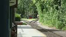 A switch track adjacent to the railroad station platform with a workman and maintenance vehicle in the background